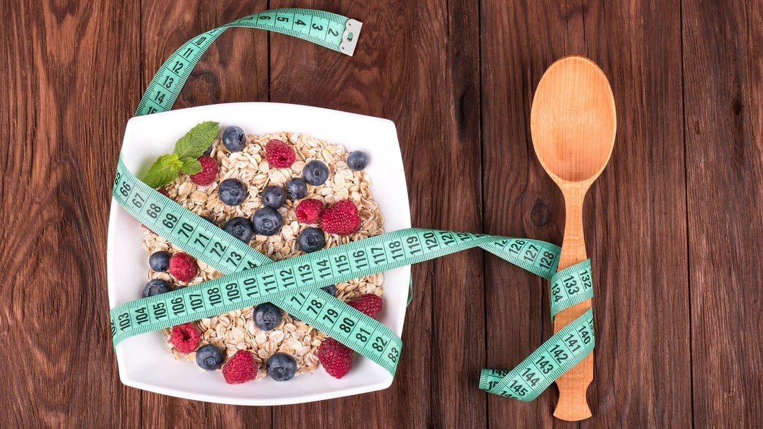 A bowl of porridge with blueberries and raspberries, wrapped with a tape measure, sits next to a wooden spoon on a wooden surface.