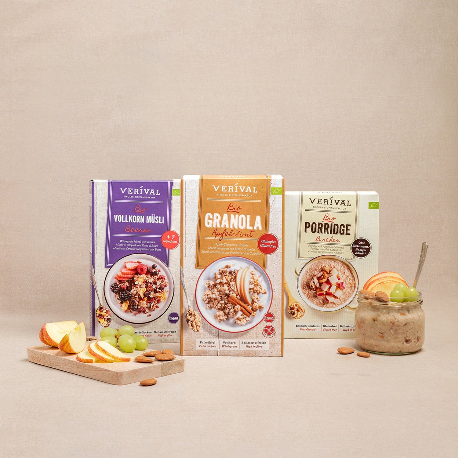 Three boxes of Verival breakfast products: wholegrain muesli, granola, and porridge, presented with fresh fruit and nuts on a beige background.