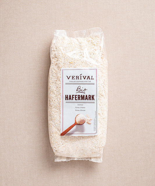 Auf neutralem Hintergrund ist eine Packung von ballaststoffreichem Hafermark von Verival Bioabgebildet. Die Verpackung ziert elegant einen Holzlöffel mit Hafermark, ideal zum Verfeinern des morgendlichen Porridges.