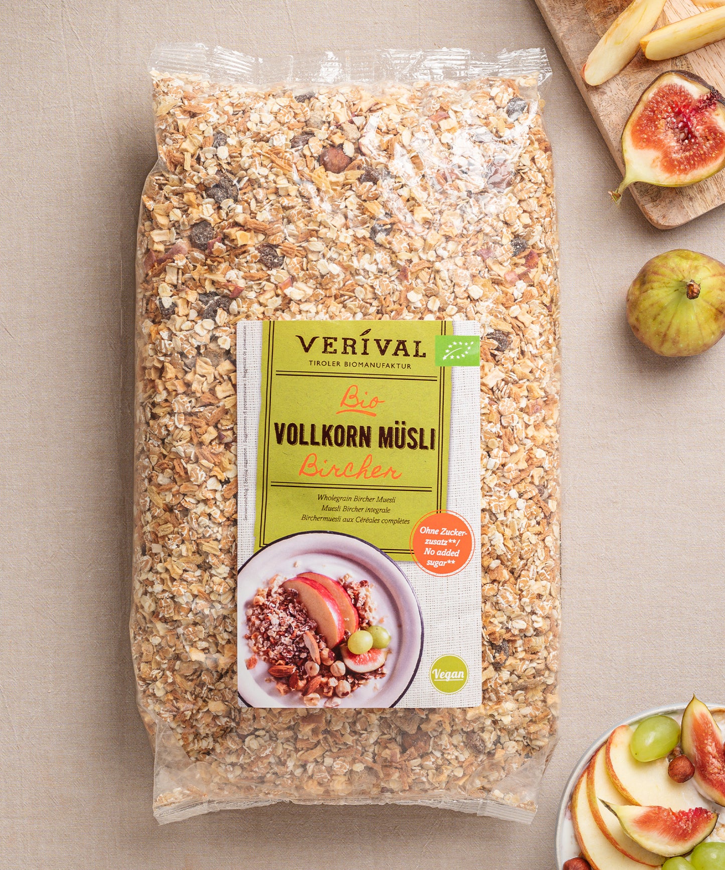 Eine Packung ballaststoffreiches Bircher Vollkorn Müsli von Verival Bio steht einladend neben einem Teller mit Apfelscheiben und Feigen auf dem Tisch.