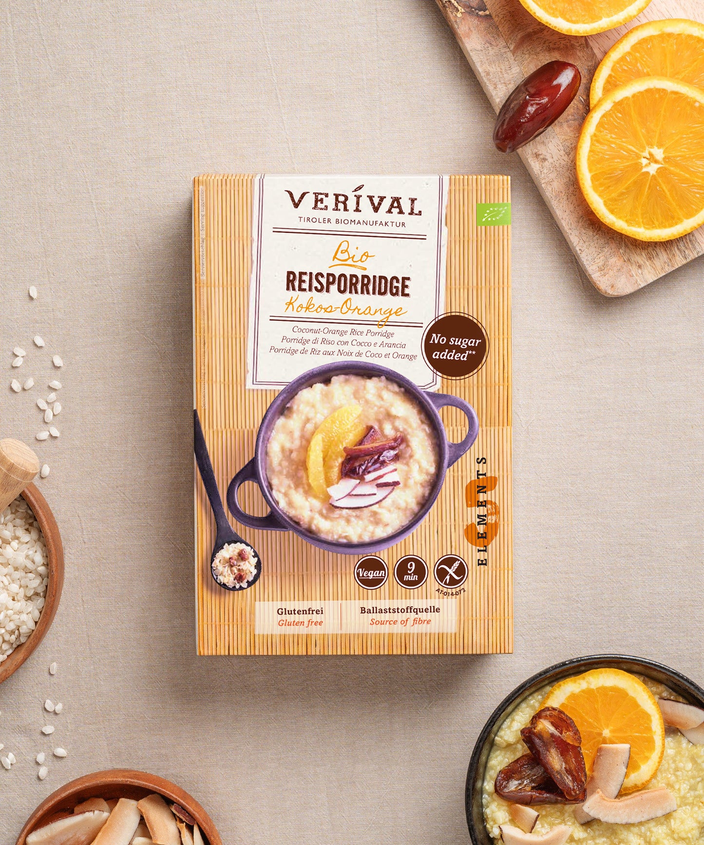 Der Kokos-Orangen-Reisporridge von Verival Bio, hergestellt nach TCM-Prinzipien, präsentiert sich mit Orangenscheiben und Datteln auf einem beigen Tuch. Glutenfreier Reis, Kokosraspeln und frisches Obst sorgen für einen nährstoffreichen Start in den Tag.