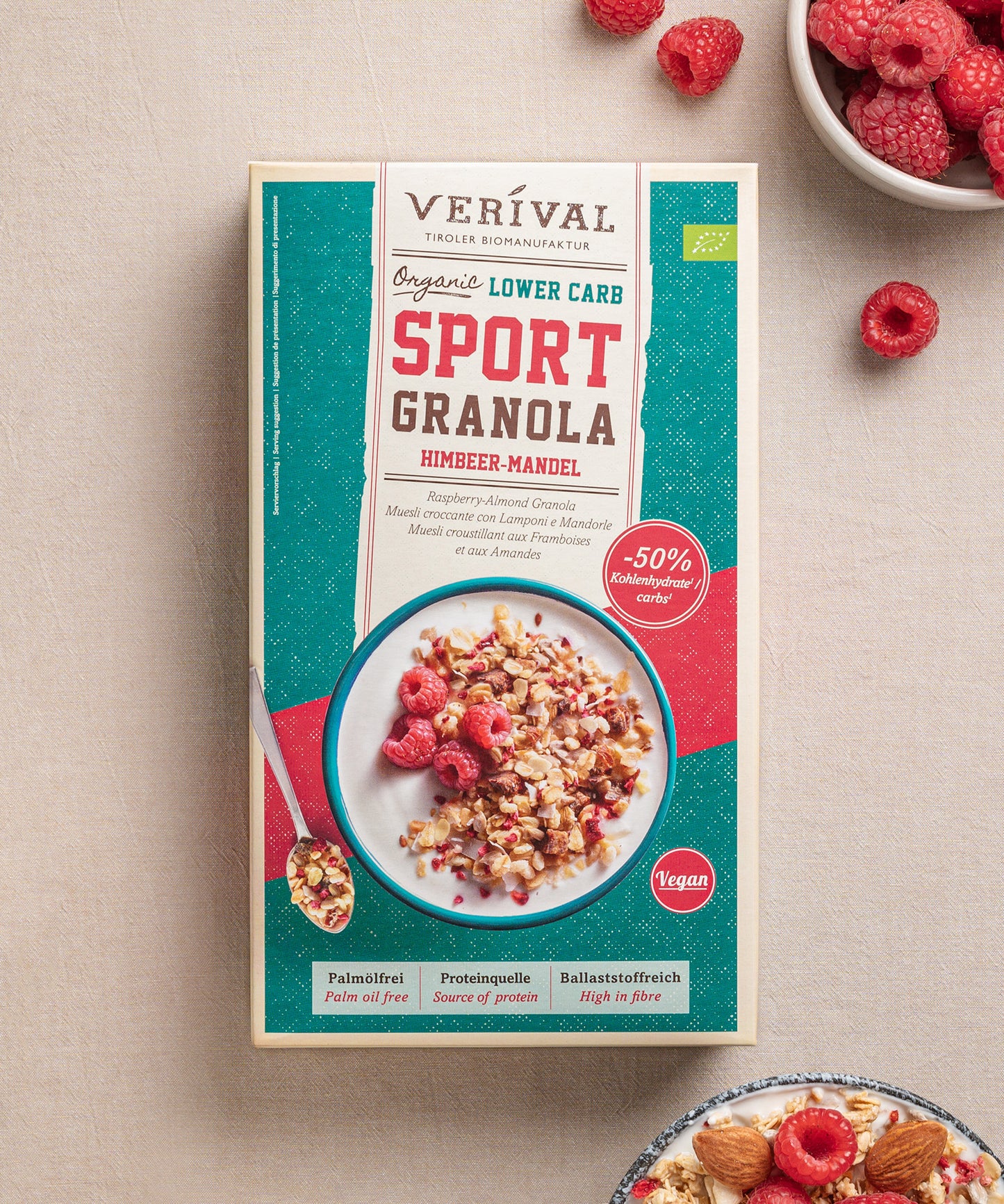 Eine Packung Protein Lower Carb Granola Himbeer-Mandel von Verival Bio, das reich an pflanzlichem Protein ist zeigt Himbeeren und Mandeln auf dem Cover und präsentiert sich neben frischen Himbeeren und einer Granola-Schale.