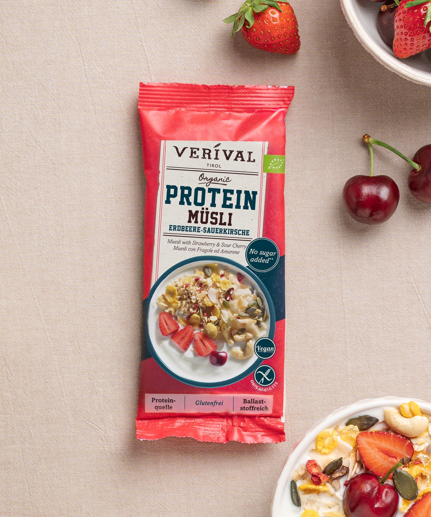 Die Einzeloportionspackung Protein Müsli Erdbeere-Sauerkirsche von Verival Bio hat eine leuchtend roten Verpackung mit einer Abbildung frischenr Erdbeeren, Kirschen und einer Schüssel Müsli daneben – eine ideale pflanzliche Proteinquelle für einen gesunden Tag.