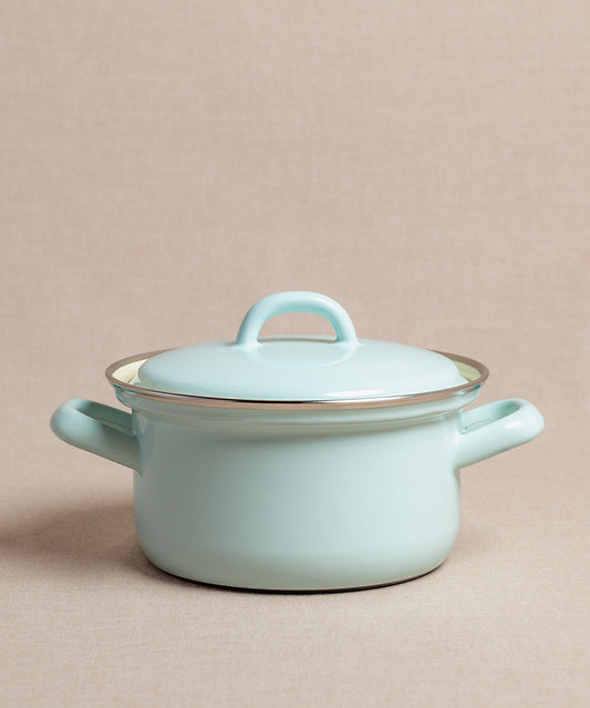 Der Porridge-Topf von Riess, ein emaillierter hellblauer Topf mit seitlichen Griffen und Deckel, steht elegant auf einer neutralen Oberfläche und eignet sich ideal zum Kochen von Haferbrei.