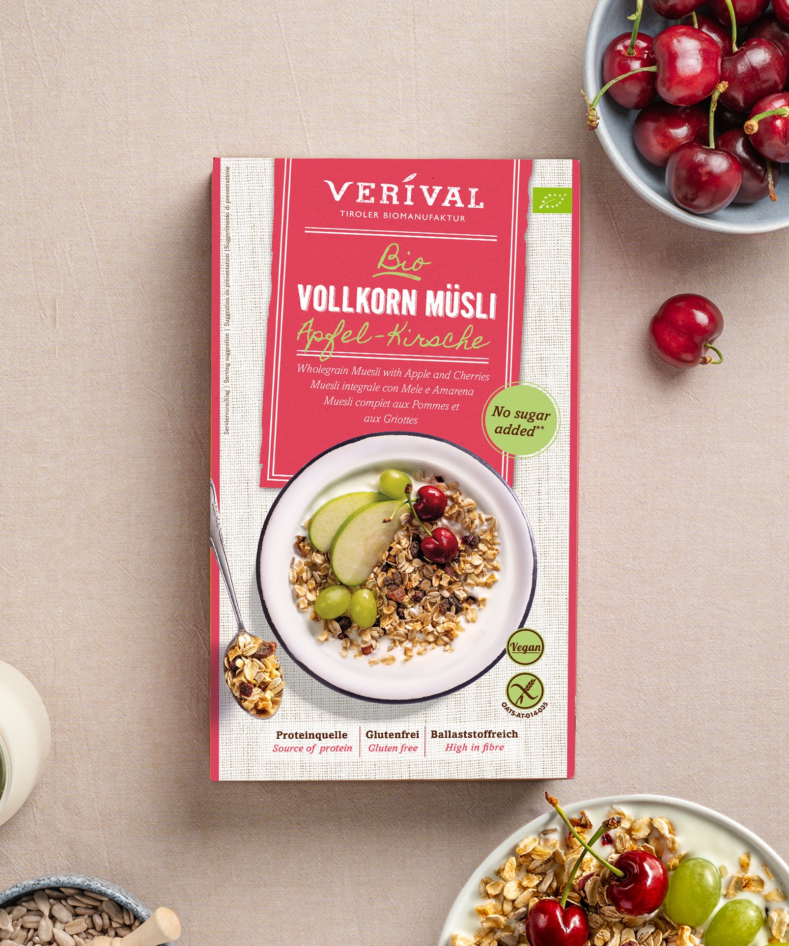 Eine Packung Apfel-Kirsch Vollkorn Müsli von Verival Bio, umgeben von Kirschen, einer Schüssel mit Müsli, garniert mit grünen Äpfeln und Trauben. Nährwertreich und ballaststoffreich – der perfekte Start in den Tag.