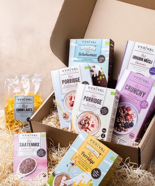 Das Set „Best Breakfast Friends“ von Verival Bio mit verschiedenen Frühstücks-Müslis, Bio-Cornflakes und Porridges in verschiedenen Geschmacksrichtungen auf einem Strohbett wird attraktiv in einem offenen Karton präsentiert.