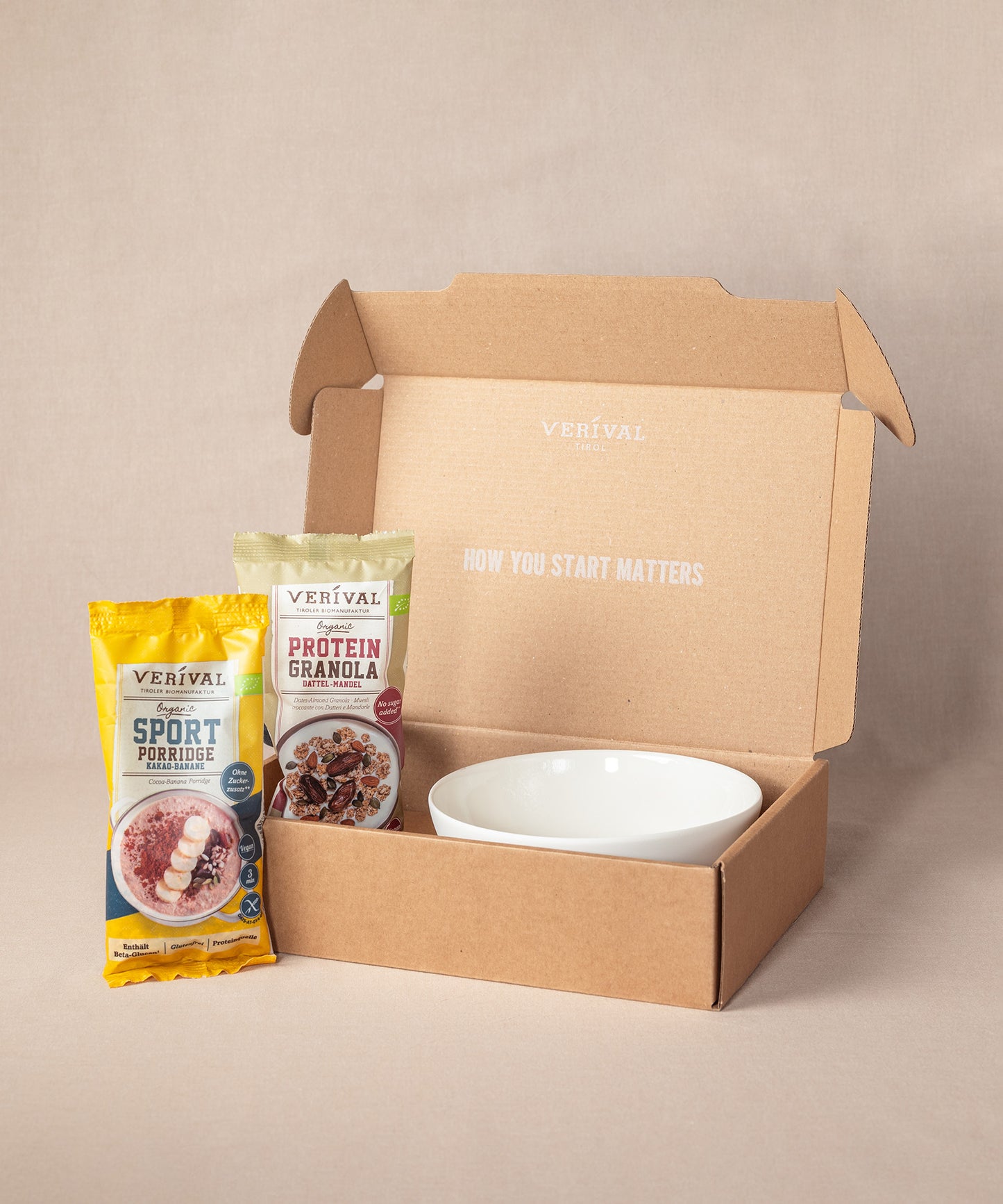 Eine geöffnete Box mit einer Porridge-Schüssel und Päckchen Verival Sport Porridge (gelb) und Protein Granola (kastanienbraun). Auf dem Deckel des Verival„Breakfast Lover“-Sets steht: „How you start matters“ – ideal für ein proteinreiches Frühstück.