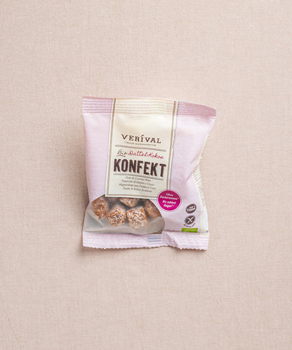 Eine Packung Dattel-Kokos Konfekt von Verival Bio liegt auf einem beigen Untergrund. Das Produkt ist eine gesunde Alternative bei Heißhunger auf Süßes.